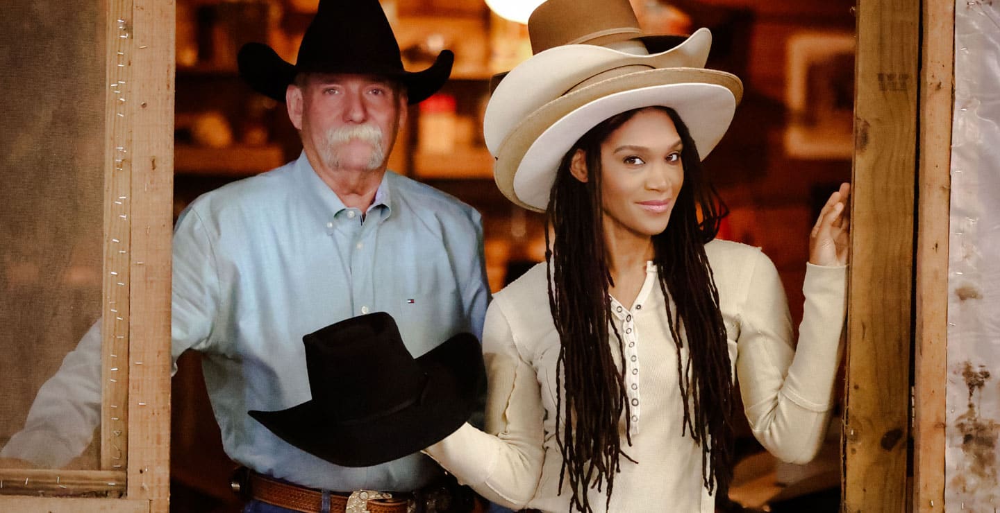 A photo of a cowboy wearing a black cowboy hat, with a woman wearing four light-colored hats, posing.